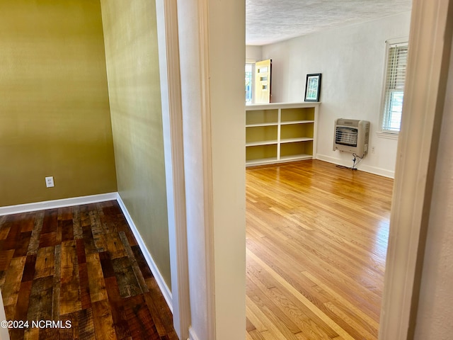 hall with a textured ceiling, heating unit, and wood-type flooring