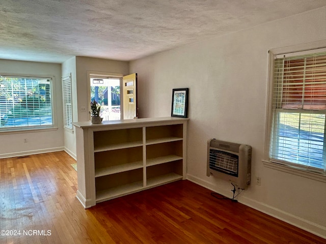 interior space with a wealth of natural light, a textured ceiling, heating unit, and hardwood / wood-style flooring