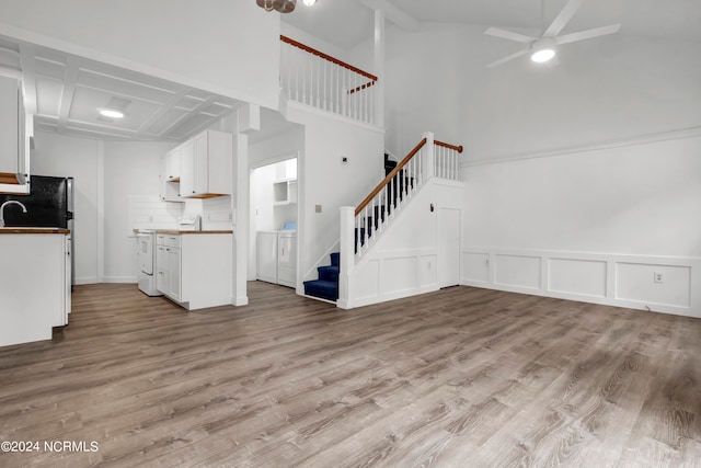 unfurnished living room with ceiling fan, washing machine and clothes dryer, beamed ceiling, a high ceiling, and light hardwood / wood-style floors