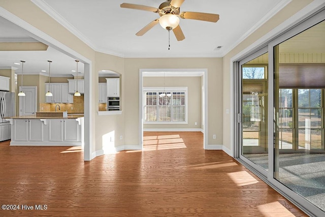 unfurnished living room featuring a wealth of natural light, crown molding, ceiling fan, and light wood-type flooring