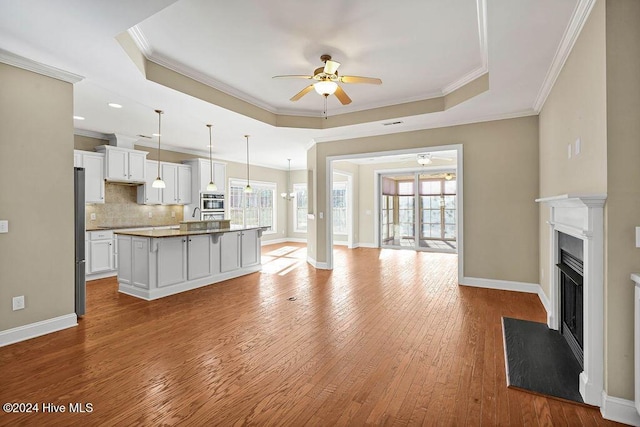 unfurnished living room with light hardwood / wood-style flooring, a raised ceiling, ceiling fan, and crown molding