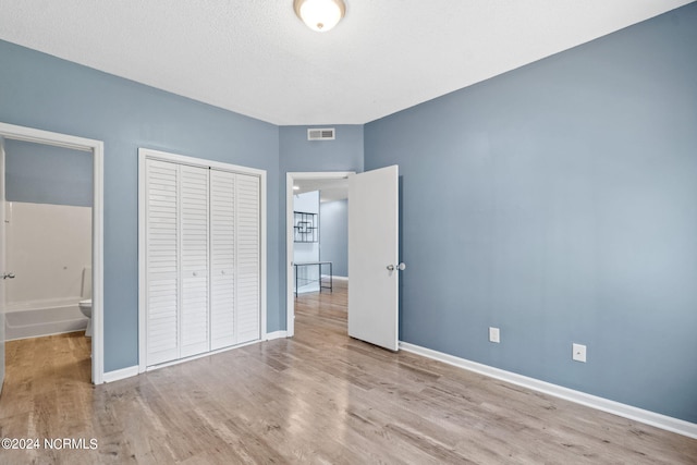 unfurnished bedroom with a closet, a textured ceiling, light wood-type flooring, and ensuite bath