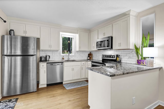 kitchen featuring light wood-type flooring, a sink, stainless steel appliances, dark stone counters, and a peninsula