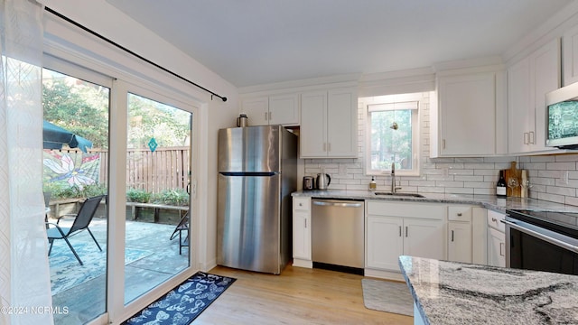 kitchen with tasteful backsplash, light stone counters, appliances with stainless steel finishes, white cabinets, and a sink