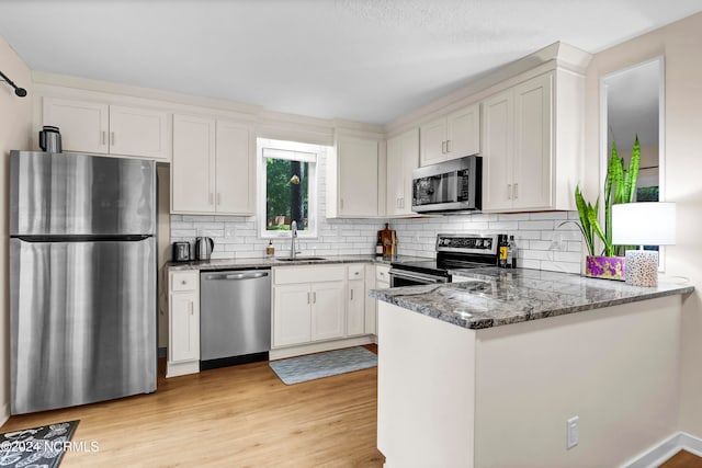 kitchen with appliances with stainless steel finishes, sink, kitchen peninsula, white cabinets, and light hardwood / wood-style flooring