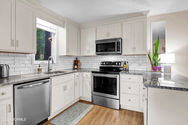 kitchen featuring dark stone countertops, light wood-style flooring, a sink, appliances with stainless steel finishes, and white cabinetry