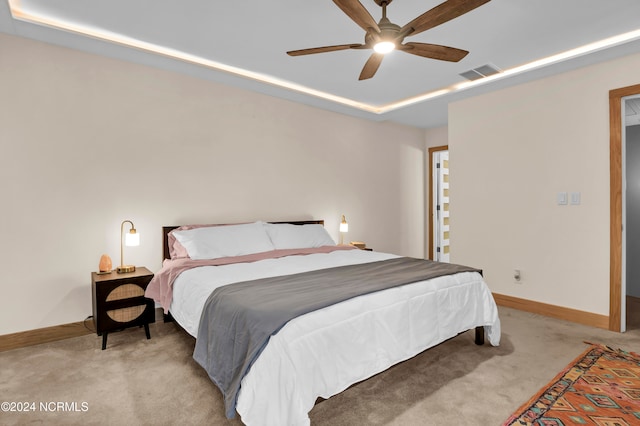 bedroom with a ceiling fan, visible vents, baseboards, a tray ceiling, and light colored carpet