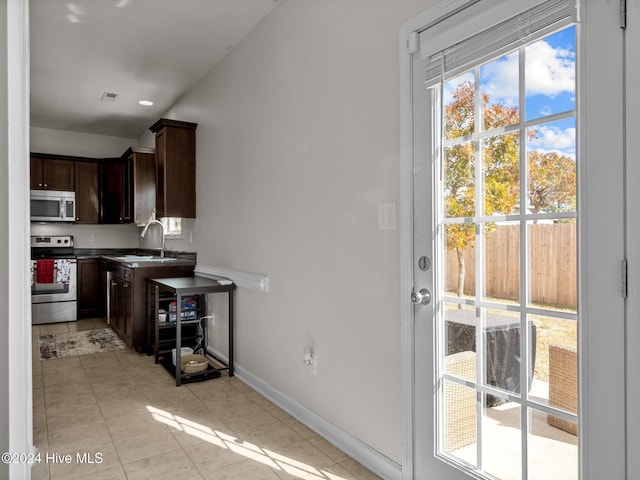 kitchen with dark brown cabinets, stainless steel appliances, light tile patterned floors, and sink