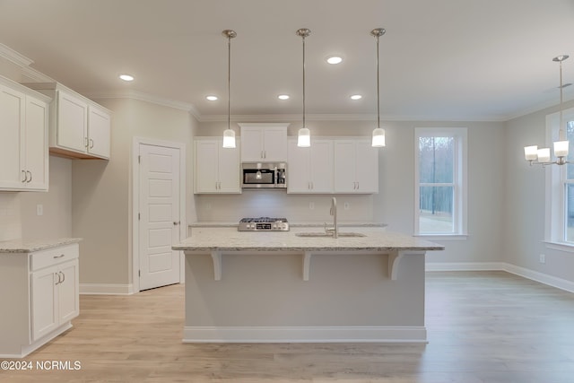 kitchen featuring white cabinets, stainless steel appliances, hanging light fixtures, and an island with sink