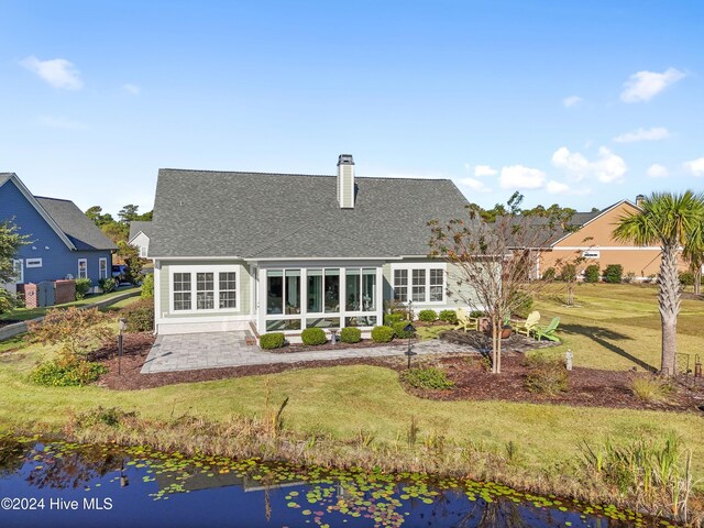 rear view of house featuring a water view, a sunroom, and a lawn