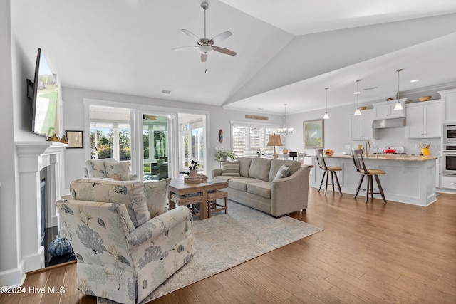 living room with light hardwood / wood-style floors, high vaulted ceiling, ceiling fan with notable chandelier, and plenty of natural light