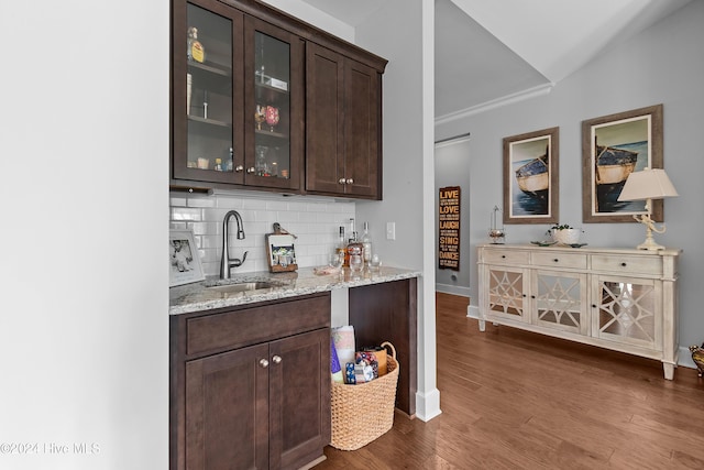 bar featuring dark hardwood / wood-style floors, backsplash, sink, dark brown cabinetry, and light stone counters