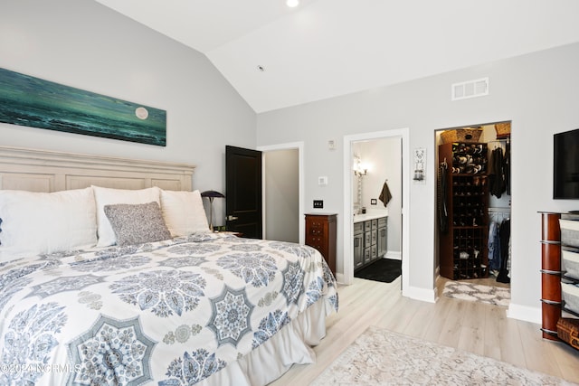 bedroom featuring a spacious closet, a closet, light hardwood / wood-style floors, vaulted ceiling, and connected bathroom