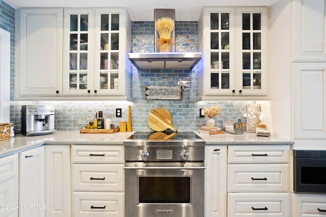 kitchen with light stone countertops, wall chimney exhaust hood, stainless steel range, white cabinets, and decorative backsplash