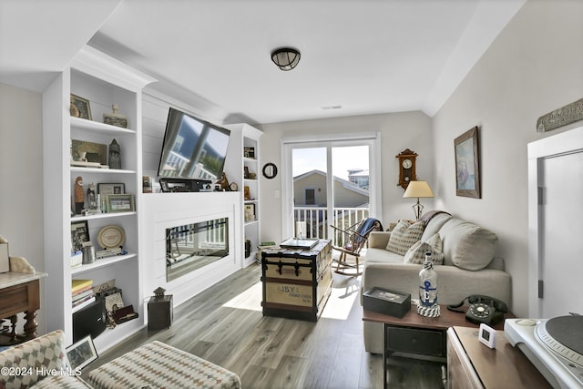 living room featuring built in shelves, wood finished floors, and a glass covered fireplace