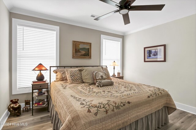 bedroom with hardwood / wood-style floors, ceiling fan, ornamental molding, and multiple windows