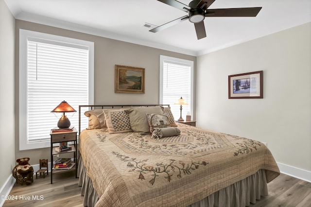 bedroom with ornamental molding, visible vents, baseboards, and wood finished floors