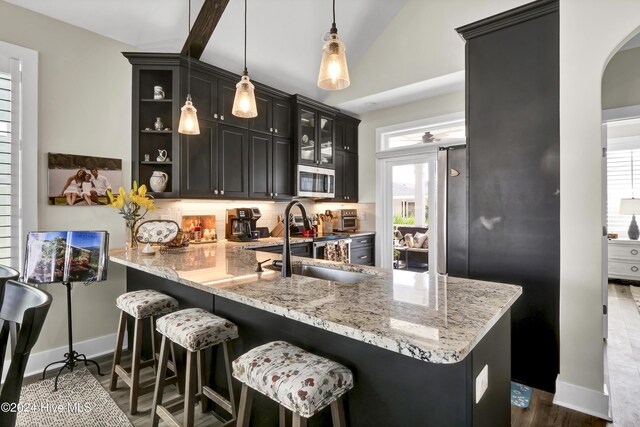 kitchen with kitchen peninsula, light stone countertops, sink, pendant lighting, and lofted ceiling