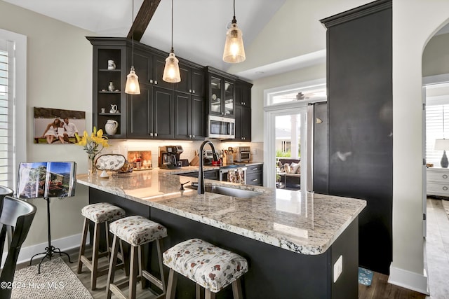 kitchen featuring decorative light fixtures, a peninsula, a sink, stainless steel microwave, and glass insert cabinets