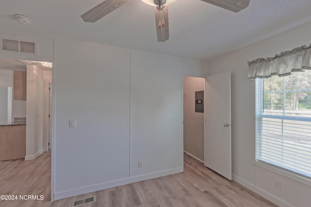 unfurnished room with light hardwood / wood-style flooring, a textured ceiling, electric panel, and ceiling fan