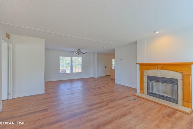 unfurnished living room with ceiling fan, a textured ceiling, light wood-type flooring, and a tile fireplace