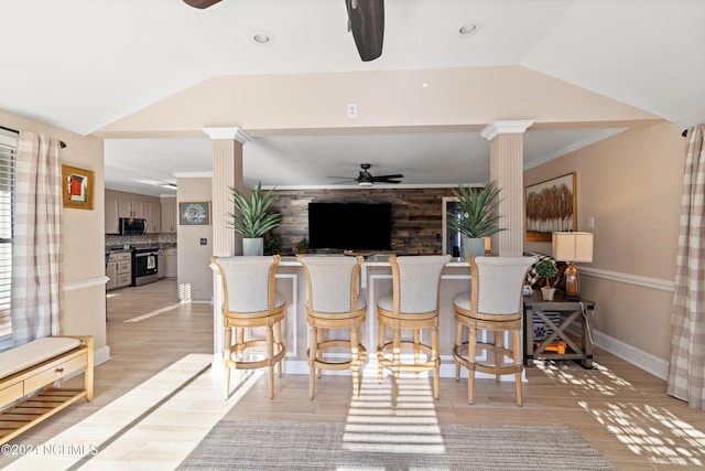 interior space featuring decorative columns, ornamental molding, lofted ceiling, and light wood-type flooring