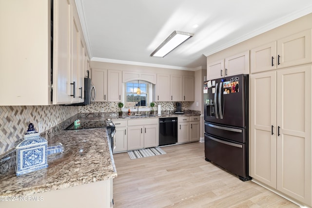 kitchen with backsplash, light stone counters, ornamental molding, black appliances, and light hardwood / wood-style flooring