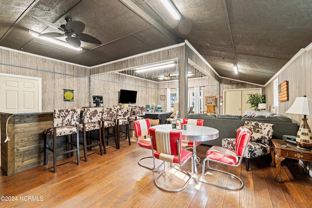 dining room with ceiling fan, wood walls, wood-type flooring, and lofted ceiling