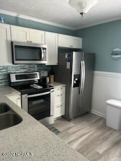 2196 New River Inlet Rd Unit 170, North Topsail Beach, NC 28460 - kitchen with appliances with stainless steel finishes, white cabinetry, light wood finished floors, a wainscoted wall, and decorative backsplash