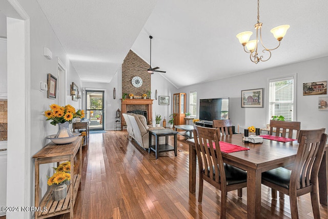 dining space with dark hardwood / wood-style flooring, lofted ceiling, ceiling fan with notable chandelier, and a brick fireplace