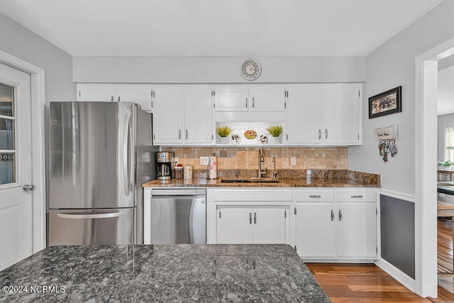 kitchen featuring appliances with stainless steel finishes, sink, white cabinetry, light hardwood / wood-style floors, and dark stone counters