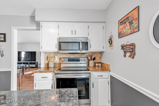 kitchen featuring white cabinets, backsplash, appliances with stainless steel finishes, hardwood / wood-style flooring, and dark stone countertops