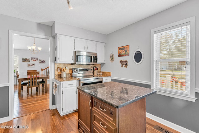 kitchen with dark stone counters, an inviting chandelier, white cabinetry, appliances with stainless steel finishes, and light hardwood / wood-style floors