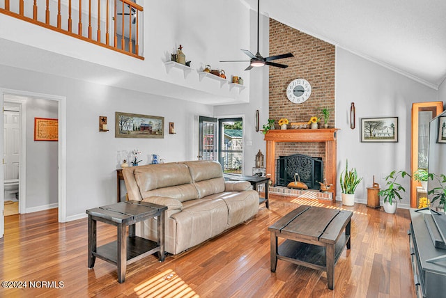 living room with ceiling fan, hardwood / wood-style flooring, high vaulted ceiling, a brick fireplace, and ornamental molding