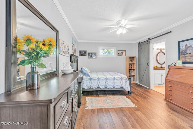 bedroom with ceiling fan, a barn door, connected bathroom, light hardwood / wood-style flooring, and ornamental molding