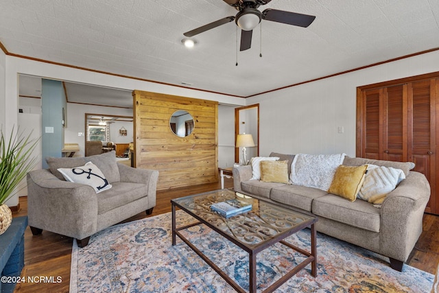 living room with ceiling fan, a textured ceiling, wood walls, ornamental molding, and dark wood-type flooring