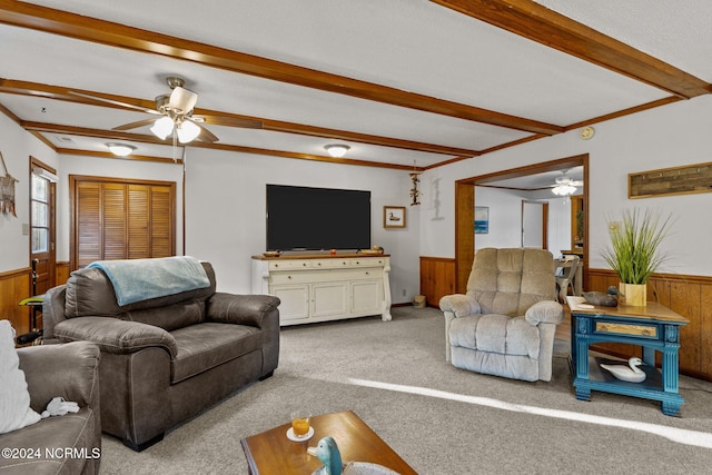 carpeted living room featuring beamed ceiling, wooden walls, and ceiling fan