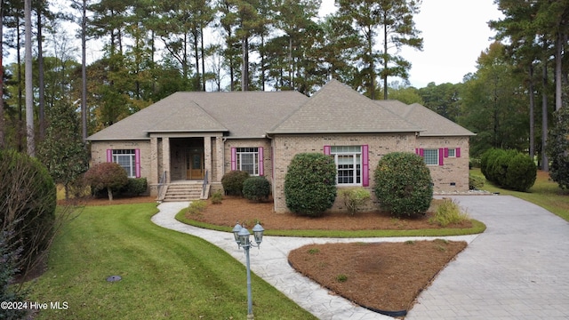 view of front facade featuring brick siding, driveway, a shingled roof, and a front yard