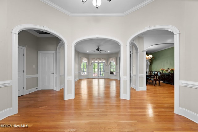 interior space with arched walkways, ornamental molding, light wood finished floors, and ceiling fan with notable chandelier