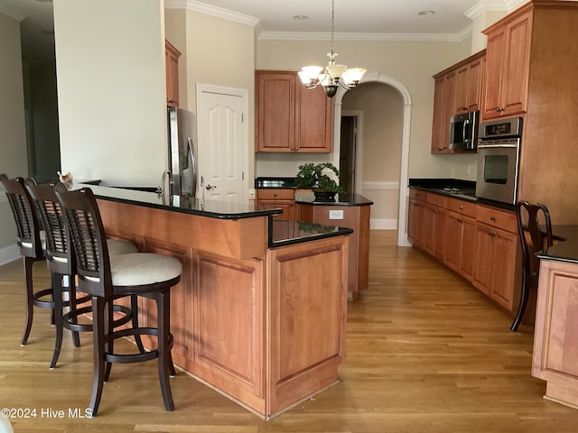 kitchen featuring an island with sink, appliances with stainless steel finishes, ornamental molding, and pendant lighting