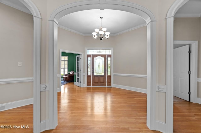entrance foyer with light wood finished floors, arched walkways, decorative columns, a notable chandelier, and ornamental molding