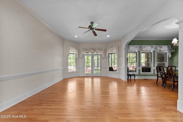 unfurnished living room with ornamental molding, arched walkways, light wood-style floors, baseboards, and ceiling fan with notable chandelier
