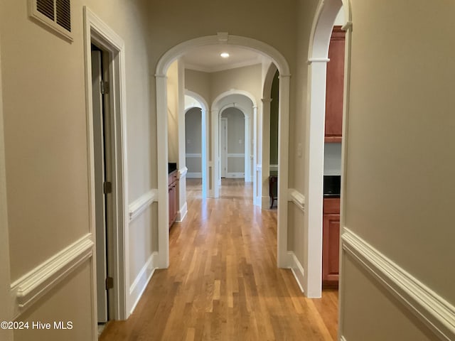 corridor with ornamental molding and light hardwood / wood-style floors