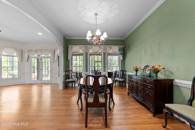 dining area with arched walkways, light wood-type flooring, crown molding, and a notable chandelier