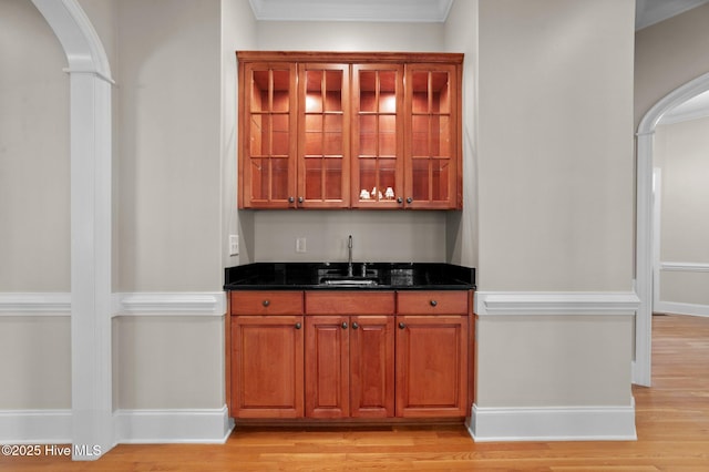 bar with indoor wet bar, arched walkways, a sink, and light wood-style floors
