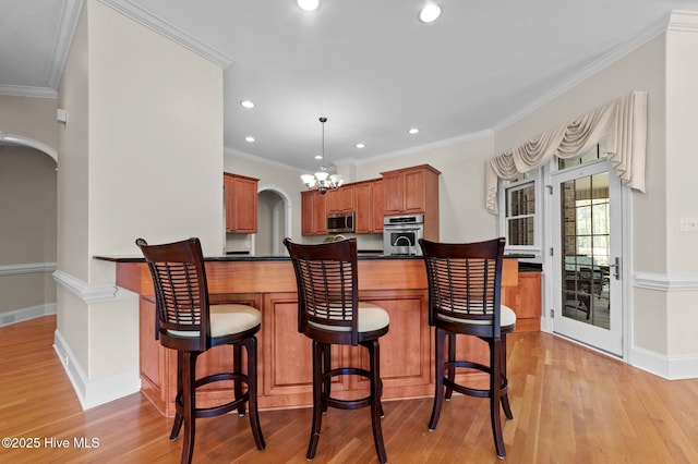 kitchen with dark countertops, light wood-type flooring, arched walkways, appliances with stainless steel finishes, and recessed lighting