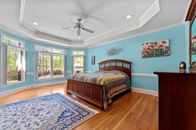 bedroom with baseboards, wood finished floors, a tray ceiling, and ornamental molding