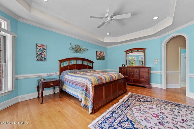 bedroom featuring light wood-style flooring, arched walkways, a raised ceiling, baseboards, and ornamental molding