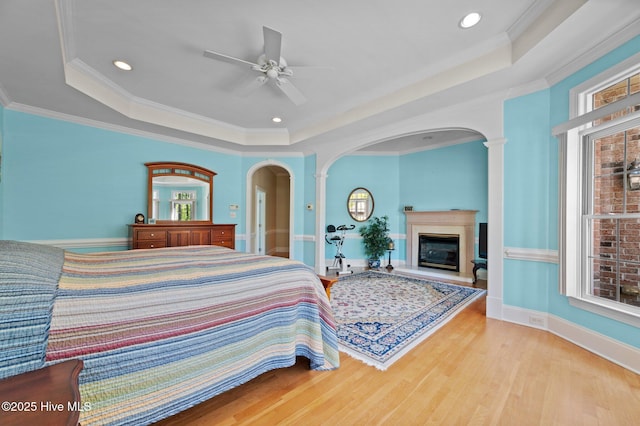 bedroom featuring a glass covered fireplace, a tray ceiling, and arched walkways