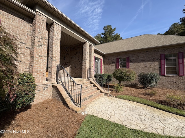 property entrance with board and batten siding, a shingled roof, a porch, and brick siding